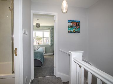 A hallway with a staircase railing and a doorway leading to a bedroom with a window at Chesil Retreat in Weymouth