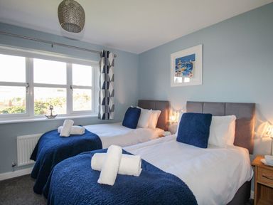 A bedroom with two single beds with blue pillows and blankets and white towels at Chesil Retreat in Weymouth