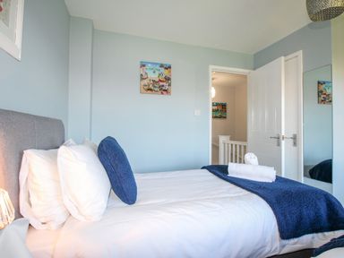 A bedroom with a made bed with white and blue bedding a door open to a hallway at Chesil Retreat in Weymouth