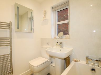 A bathroom with a toilet sink bathtub mirror towel rack and window at Chesil Retreat in Weymouth