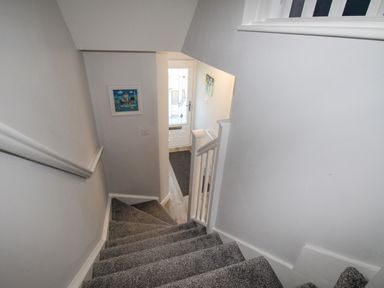 A staircase with carpeted steps leading down to a white front door with decorative glass at Chesil Retreat in Weymouth