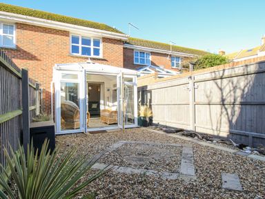 A backyard with gravel ground and a conservatory with wicker chairs at Chesil Retreat in Weymouth