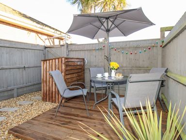 A small fenced patio with a round table four chairs an umbrella and string lights at Chesil Retreat in Weymouth