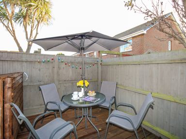 A small outdoor patio area with a round glass table and four chairs under a large umbrella at Chesil Retreat in Weymouth
