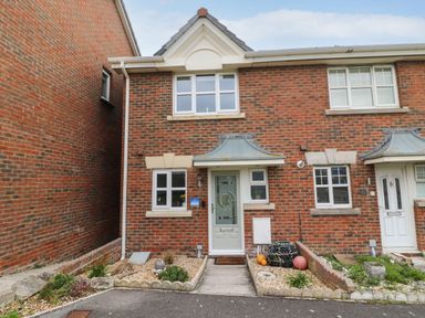 A brick two storey house with a white front door and small garden beds at Chesil Retreat in Weymouth