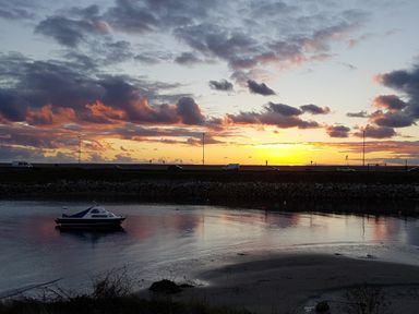 A small boat on water near a rocky shore at sunset with cars on a road in the background at Chesil Retreat Weymouth