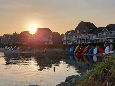 A row of houses behind a shoreline with kayaks and boats lined up at Chesil Retreat in Weymouth