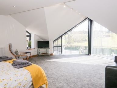 A bedroom with a bed a chair a small table a television and large windows at The Annexe in Llanfairpwllgwyngyll