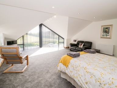 A bedroom with a bed a black sofa a wooden armchair a television and large triangular windows at The Annexe in Llanfairpwllgwyngyll