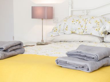 A bed with floral bedding and folded grey towels with a bedside lamp on a table at The Annexe in Llanfairpwllgwyngyll