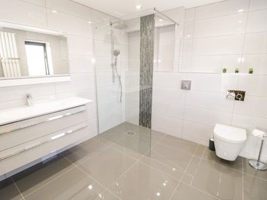 A bathroom with a wall-mounted sink and vanity mirror a walk-in shower with glass partition and a wall-mounted toilet at The Annexe in Llanfairpwllgwyngyll