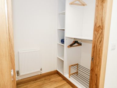 A walk-in closet with white shelving and hangers and a wooden floor at The Annexe in Llanfairpwllgwyngyll