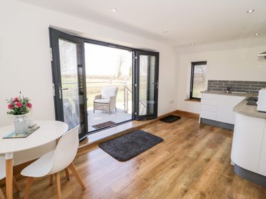 A kitchen with wooden floor a small round table with chairs flowers on the table and open patio doors leading outside at The Annexe in Llanfairpwllgwyngyll