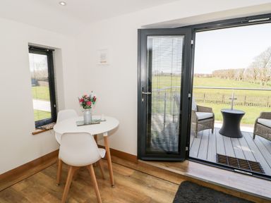 A dining area with a round white table and two white chairs next to a glass door opening to a patio with wicker chairs and a small table at The Annexe in Llanfairpwllgwyngyll