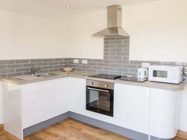 A kitchen with white cabinets a built in oven a stovetop a microwave a kettle a sink and gray tiled backsplash at The Annexe in Llanfairpwllgwyngyll