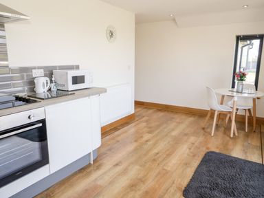 A kitchen area with a microwave kettle and stove next to a small dining table with two chairs and flowers at The Annexe in Llanfairpwllgwyngyll