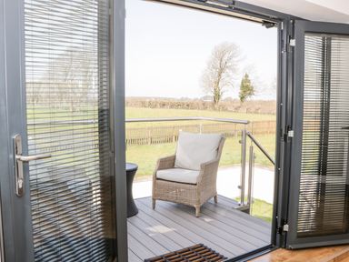 A patio door opening to a balcony with a wicker chair and a small table overlooking a grassy field at The Annexe in Llanfairpwllgwyngyll