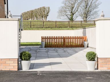 A paved outdoor area with potted plants and a wooden fence in front of a grassy area at The Annexe in Llanfairpwllgwyngyll