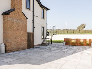 An outdoor patio area with tiled flooring next to a two-story house with an external metal staircase and a wooden fence at The Annexe in Llanfairpwllgwyngyll