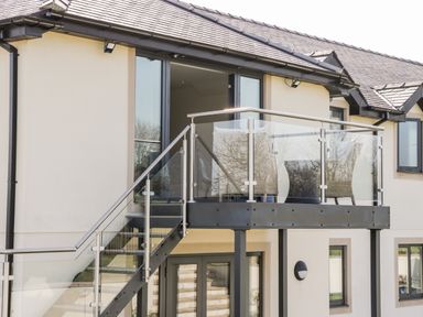 An outdoor balcony with glass railing and two wicker chairs at The Annexe in Llanfairpwllgwyngyll