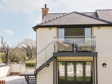 A house with a balcony and outdoor chairs with trees in the background at The Annexe in Llanfairpwllgwyngyll