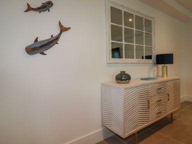 A sideboard with a vase, book, and lamp below a wall mirror and two whale sculptures on the wall at 30 Cliff Edge in Newquay