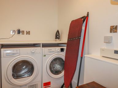 A laundry room with a washing machine dryer ironing board and iron at 30 Cliff Edge in Newquay