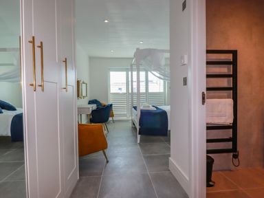 A bedroom with a canopy bed and chairs seen from a hallway near a bathroom with a towel rack at 30 Cliff Edge in Newquay