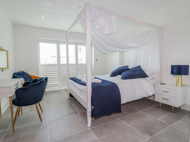 A bedroom with a four-poster bed blue cushions and throw a desk with a chair and a bedside table with a lamp at 30 Cliff Edge in Newquay