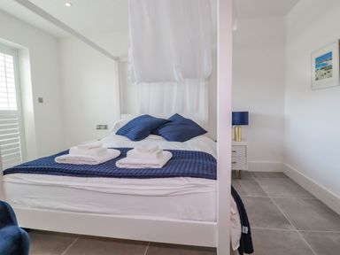 A bedroom with a white four-poster bed with blue pillows and folded towels and a nightstand with a blue lamp at 30 Cliff Edge in Newquay