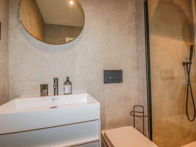 A bathroom with a white sink faucet round mirror and shower area at 30 Cliff Edge in Newquay