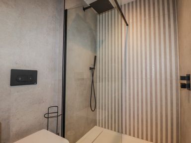 A bathroom with a walk-in shower with a glass door and a striped wall at 30 Cliff Edge in Newquay