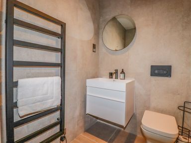 A bathroom with a towel rack toilet wall-mounted sink and round mirror at 30 Cliff Edge in Newquay