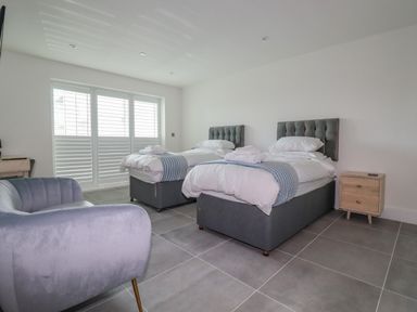 A bedroom with two single beds a grey armchair and a wooden nightstand at 30 Cliff Edge in Newquay