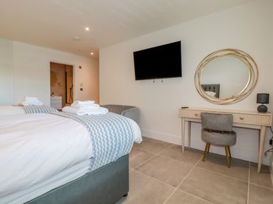 A bedroom with two beds a wall-mounted television a desk with a chair and a round mirror at 30 Cliff Edge in Newquay