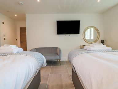 A bedroom with two beds a wall mounted television a round mirror and a small grey sofa at 30 Cliff Edge in Newquay