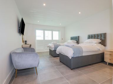 A bedroom with two single beds gray headboards gray armchair wall mounted tv and large windows with shutters at 30 Cliff Edge in Newquay
