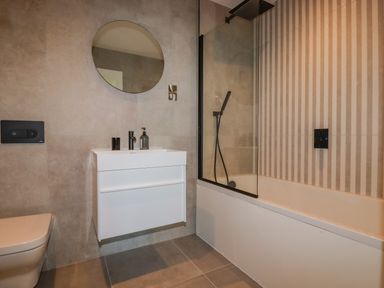 A bathroom with a wall-mounted sink and mirror next to a bathtub with a glass shower screen at 30 Cliff Edge in Newquay