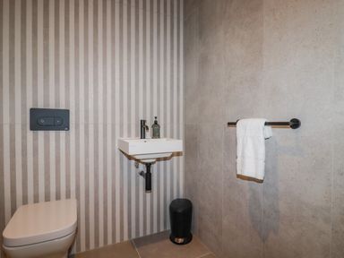 A bathroom with a toilet a small wall-mounted sink a towel rack with a white towel and a black trash bin at 30 Cliff Edge in Newquay