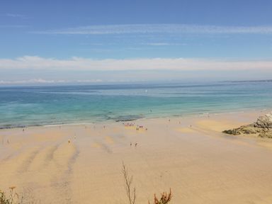 A sandy beach with people near the shoreline and calm ocean waters at 30 Cliff Edge in Newquay