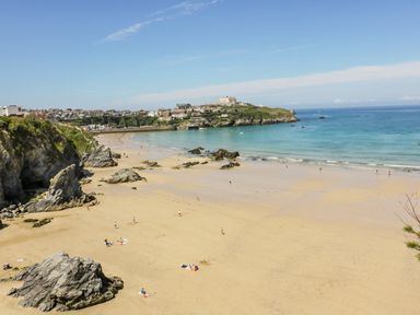 A sandy beach with rocks and people near a coastal town and blue ocean at 30 Cliff Edge in Newquay