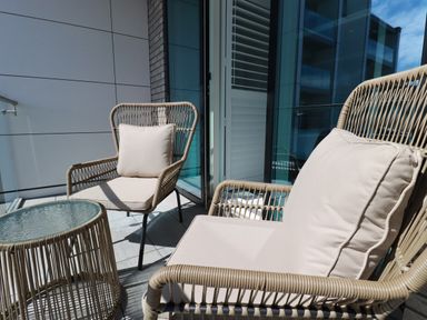 Two wicker chairs with cushions and a small glass top table on a balcony at 30 Cliff Edge in Newquay
