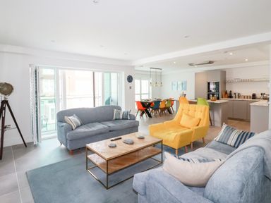 A living room with blue sofas a yellow armchair and a wooden coffee table next to a dining area with colorful chairs at 30 Cliff Edge in Newquay