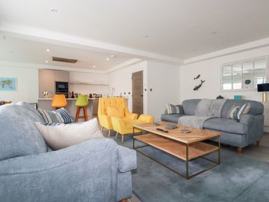 A living room with blue sofas yellow armchairs a wooden coffee table and colorful bar stools at 30 Cliff Edge in Newquay