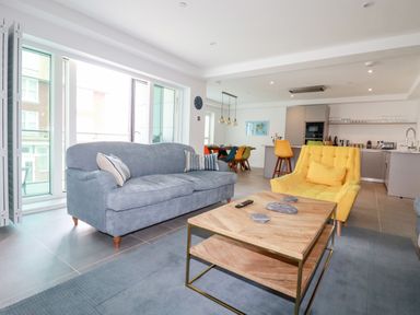 A living room with a gray sofa and a yellow armchair a wooden coffee table and an open kitchen with a dining table at 30 Cliff Edge in Newquay
