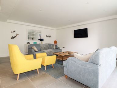 A living room with two grey sofas one yellow armchair and ottoman a wooden coffee table and a wall-mounted TV at 30 Cliff Edge in Newquay