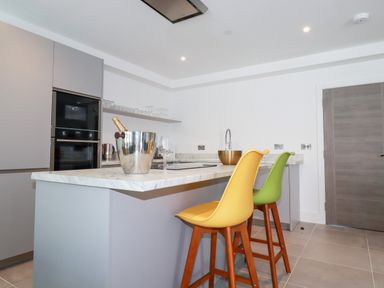 A kitchen with a marble countertop island yellow and green bar stools and a champagne bucket at 30 Cliff Edge in Newquay