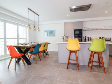 A kitchen and dining area with colorful chairs around a wooden table and bar stools at 30 Cliff Edge in Newquay