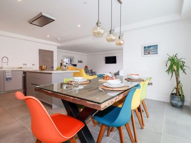A dining area with a glass top wooden table surrounded by colorful chairs in a kitchen and living room space at 30 Cliff Edge in Newquay