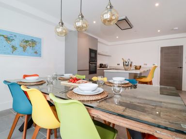 A kitchen and dining area with a glass table set with plates and colorful chairs at 30 Cliff Edge in Newquay